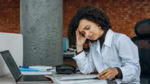 Woman feeling stressed while working on a laptop, representing effects of screen time on skin.