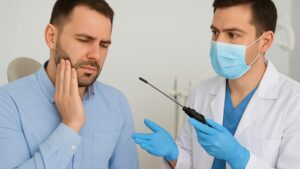 Male maxillofacial surgeon explaining TMJ arthroscopy procedure to a patient with jaw pain during consultation.