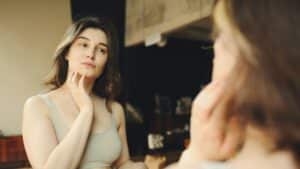 Woman examining her facial skin for pigmentation and uneven tone in front of a mirror
