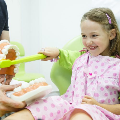 Girl in dentists chair toothbrushing a model Pandit Clinic Child's First Dental Visit